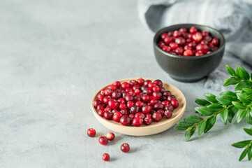 Fresh cranberries in a wooden bowl on a blue background with green branch, napkin and natural light close up.