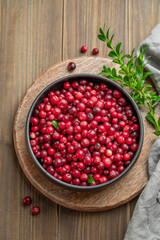 Fresh cranberries in a dark bowl on a wooden background with green branch and napkin.