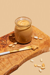 Peanut butter in a glass jar on a wooden board on a beige background