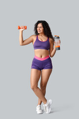 Sporty young African-American female coach with dumbbell and water bottle on white background