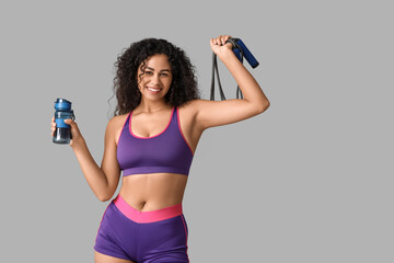 Sporty young African-American female coach with jumping rope and water bottle on white background
