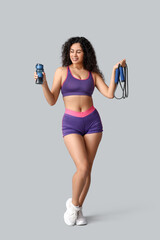 Sporty young African-American female coach with jumping rope and water bottle on white background