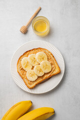 Peanut butter toast and banana in a white plate on a light background