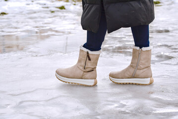 Suede boots closeup on female legs walking on dangerous icy ground with frozen puddles in winter weather, safety hazard and seasonal footwear fashion outdoors in the city