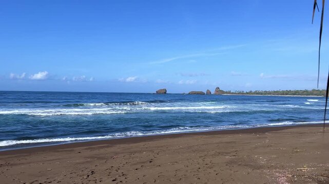 The sea in Jember, East Java. Indonesia. Watu Ulo beach with dark sand, mountains and coral rocks towering above the beach. The raging blue Indian ocean on a sunny day. 4К