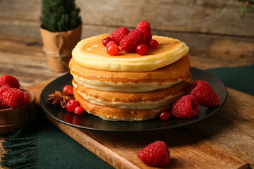 Plate of sweet pancakes with berries and Christmas tree on wooden background