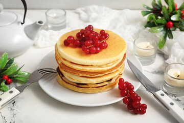 Plate of sweet pancakes with red currants, burning candles and mistletoe branches on white background