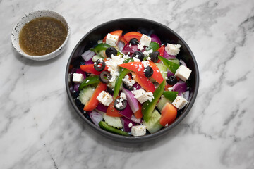 A vibrant and healthy Greek salad in a dark bowl with a small bowl of dressing