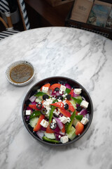A colorful and appetizing Greek salad in a dark bowl with a small bowl of dressing