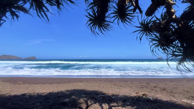 The sea in Jember, East Java. Indonesia. Watu Ulo beach with dark sand, mountains and coral rocks towering above the beach. The raging blue Indian ocean on a sunny day. 4К