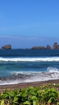 The sea in Jember, East Java. Indonesia. Watu Ulo beach with dark sand, mountains and coral rocks towering above the beach. The raging blue Indian ocean on a sunny day. 4К