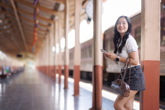 Young asian woman smiling using smartphone at train station