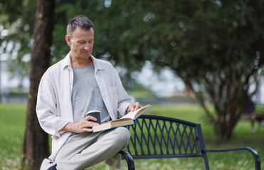 Fototapeta premium Mature man relaxing outdoor reading book and drinking coffee
