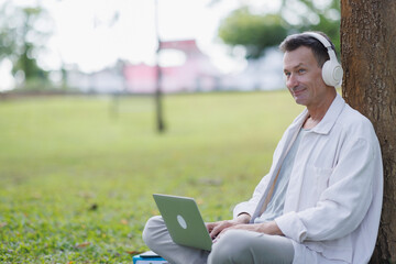 Mature man working, relaxing with laptop and headphones in park