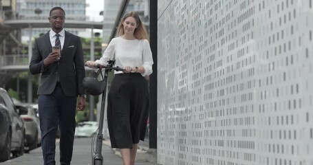 Two business colleagues commute through the city on an electric scooter, moving between sleek glass buildings toward the office and showcasing a modern, eco friendly work culture.
 - Powered by Adobe