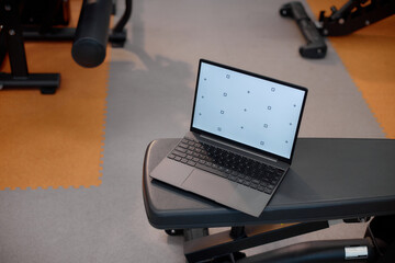 Laptop computer resting on gym bench with exercise equipment in background, screen displaying calibration marks, illustrating technology integration in fitness environment
