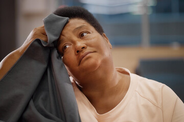 Portrait of senior Black woman resting head on hand while holding cloth against forehead, gazing...