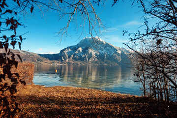 Fototapeta premium Scenic view of tranquil lake surrounded by autumn foliage and majestic mountain peaks under a clear blue sky, showcasing natural beauty and serenity
