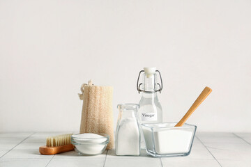 Bottle of vinegar with baking soda, spoon and cleaning supplies on tile table against white...