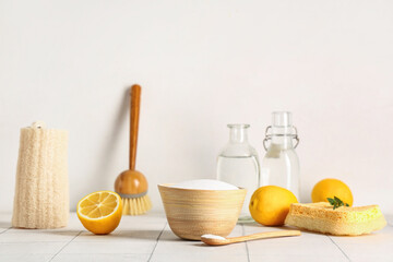 Bowl of baking soda with vinegar, lemon and cleaning supplies on tile table against white background
