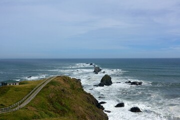 Fototapeta premium Cliffside boardwalk and sea stacks at Cape Erimo, Hokkaido — turbulent Pacific surf along rugged shoreline
