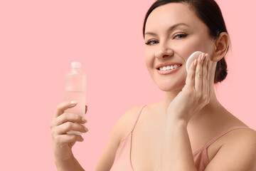 Beautiful adult woman with cotton pad applying face toner on pink background