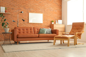 Interior of modern office with dresser, armchair and cozy orange sofa near brick wall