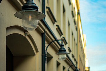 Street lamps mounted on the facade of a classical building, architectural detail of light-colored walls viewed in soft daytime lighting within city environment