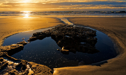 A rock pool on an empty beach nearing sunset at Kaihoka, Golden Bay, New Zealand.