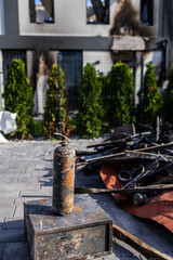 Aerial view of fire aftermath charred extinguisher and scorched debris foreground damaged building with blackened windows, green shrubs and fence frame stark contrast between destruction and recovery.