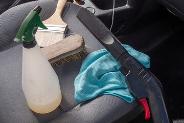 Spray bottle of cleaner sits on a seat next to a brush and a blue cloth