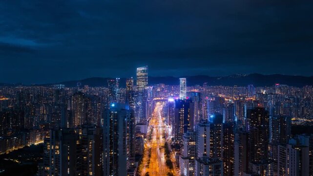 Dynamic hyper time-lapse aerial view of a vibrant modern city skyline at night with skyscrapers lighting up and traffic light trails below.