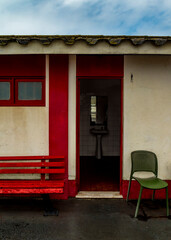 Exterior of a public restroom with a red bench and a green chair.