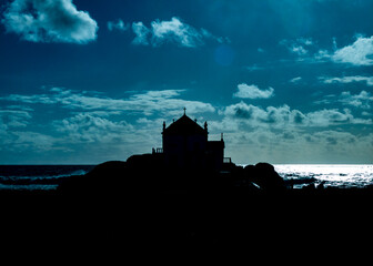 Silhouette of a church on a rocky outcrop with the ocean and sky in the background.
