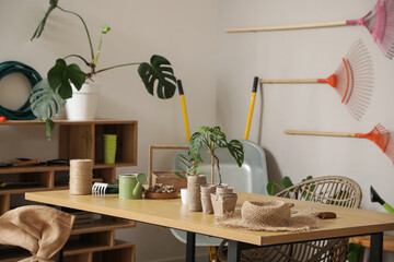 Gardener workspace with table, shelving unit and different gardening supplies near light wall,...
