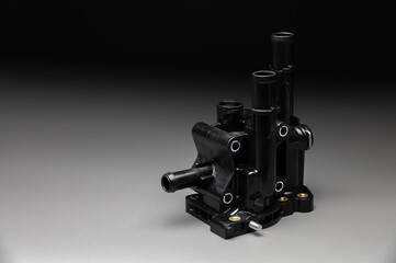 Plastic thermostat housing for the internal combustion engine cooling system. This spare part of the car's engine cooling system is on a gray gradient background.