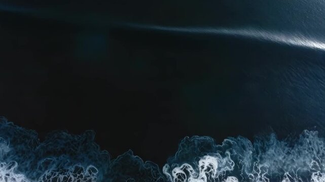 Aerial view of dark blue ocean with white foamy waves washing onto a black sand shore.