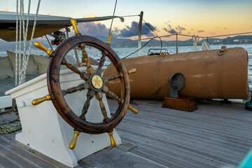 An unmanned wooden yacht wheel with gold handles glows in the Caribbean sunset, the island beyond bathed in warm light and tranquillity