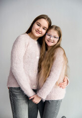 two cute beautiful sisters in pink handmade sweaters hugging in white studio