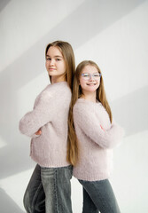 two cute beautiful sisters in pink handmade sweaters hugging in white studio