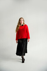 young blonde smiling beautiful lady in red handmade sweater and black skirt and black flower on the neck posing in white studio