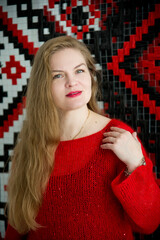 young blonde smiling beautiful lady in red handmade sweater and black skirt and black flower on the neck posing in white studio