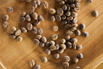 Roasted coffee beans spilling from a glass jar onto a wooden surface under warm natural light.
