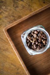 Roasted coffee beans spilling from a glass jar onto a wooden surface under warm natural light.
