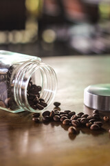 Roasted coffee beans spilling from a glass jar onto a wooden surface under warm natural light.
