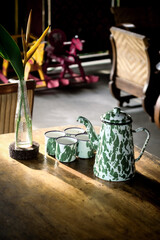 Vintage green enamel teapot and matching cups on a wooden table in a cozy rustic café, with soft natural light and blurred background.