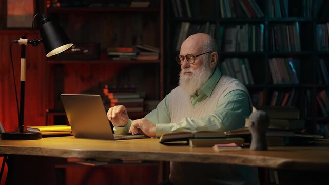 Senior male scientist typing on laptop in evening, happy with ongoing research