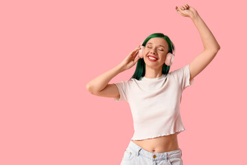 Happy young woman with green hair in headphones dancing on pink background