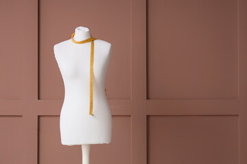 Mannequin for tailor with measuring tape on brown wooden background
