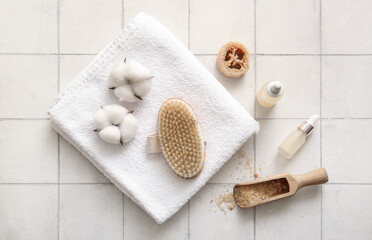 Massage brush with towel, cosmetic products and cotton flowers on white tile background